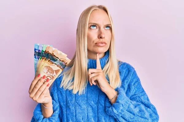 Young Blonde Girl Holding Canadian Dollars Thinking Concentrated Doubt Finger — Stock Photo, Image