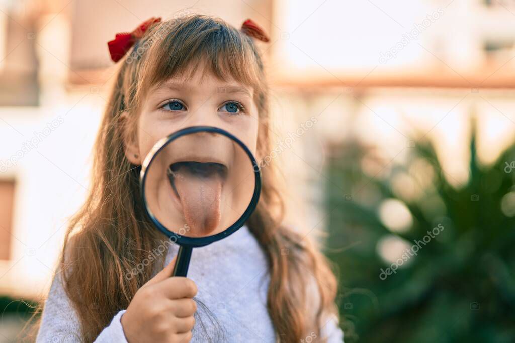 Adorable caucasian child girl with tongue out using loupe at the city.