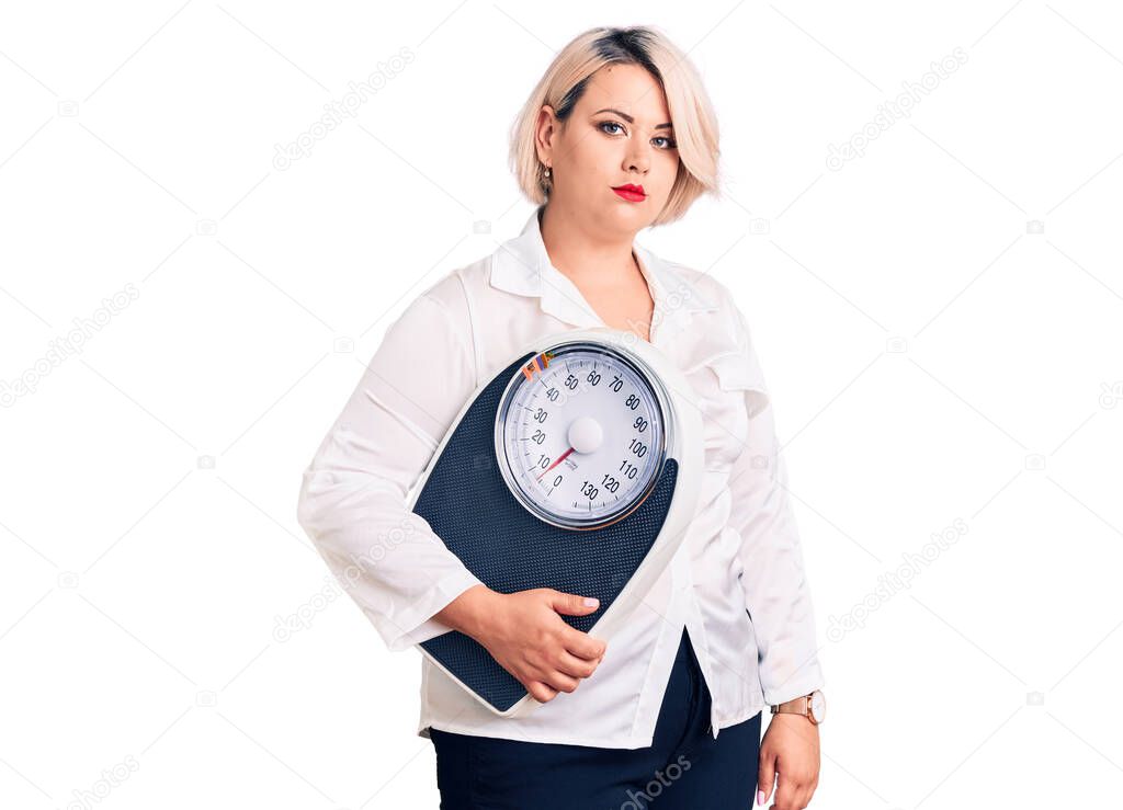 Young blonde plus size woman holding weighing machine thinking attitude and sober expression looking self confident 