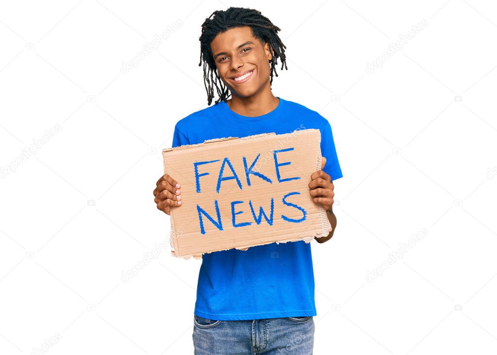 Young african american man holding fake news banner looking positive and happy standing and smiling with a confident smile showing teeth 