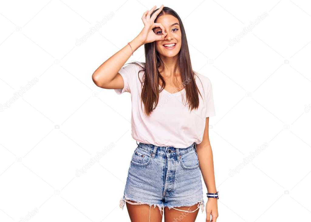 Young hispanic woman wearing casual white tshirt doing ok gesture with hand smiling, eye looking through fingers with happy face. 