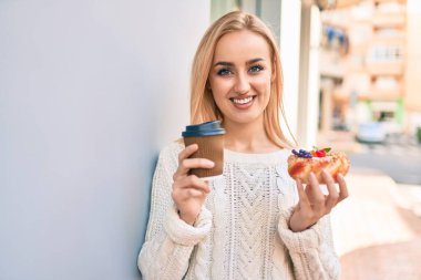 Genç sarışın kız gülümsüyor. Kahvaltıyı şehirde yaptığı için mutlu..