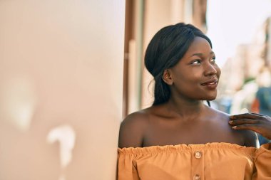 Genç Afrikalı Amerikalı kadın gülümseyerek şehirde mutlu mesut duruyor..