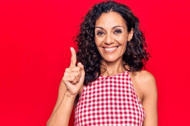 Orta yaşlı, kolsuz tişört giyen güzel bir kadın bir fikir veya soruyla gülümsüyor ve mutlu bir yüzle işaret ediyor. 