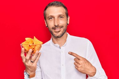 Patates cipsi tutan genç yakışıklı adam mutlu bir şekilde el ve parmak işareti yapıyor. 