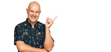 Orta yaşlı, kel, günlük kıyafetler giyen, gülümseyen, mutlu, eli ve parmağı yana doğru olan bir adam. 