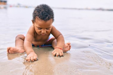 Sevimli Afro-Amerikan çocuk sahilde oturuyor..