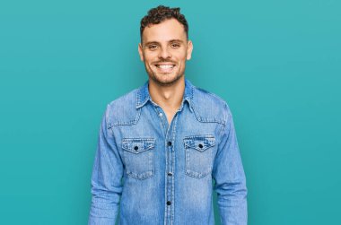 Yüzünde mutlu ve havalı bir gülümseme olan sıradan bir kot ceket giyen genç bir İspanyol. şanslı kişi. 