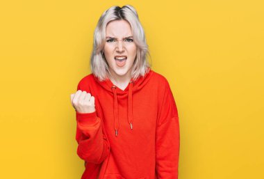 Kızgınlık ve kızgınlık içinde genç sarışın bir kız öfkeyle bağırırken yumruğunu sallıyor ve öfkeleniyor. öfke ve agresif konsept. 