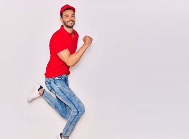 Mutlu gülümseyen üniformalı yakışıklı İspanyol teslimatçı. Yüzünde tebessümle zıplıyor, beyaz arka planda yumruklar havada kutluyor..