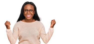 Genç siyah kadın gündelik kıyafetler ve gözlük takıyor gururla bağırıyor, zaferi kutluyor ve başarıyı kollarını kaldırarak kutluyor. 