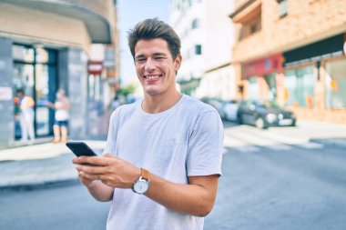 Beyaz adam şehirde akıllı telefon kullanarak mutlu bir şekilde gülümsüyor..