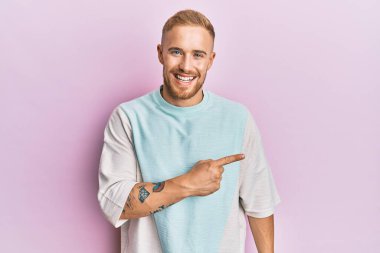 Yüzünde mutlu ve doğal bir ifade olan, el ve parmaklarıyla işaret eden, güler yüzlü, gündelik kıyafetler giyen beyaz bir genç adam. 