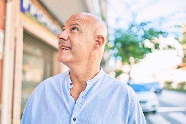 Orta yaşlı kel adam gülümseyerek şehirde mutlu mesut yürüyor..