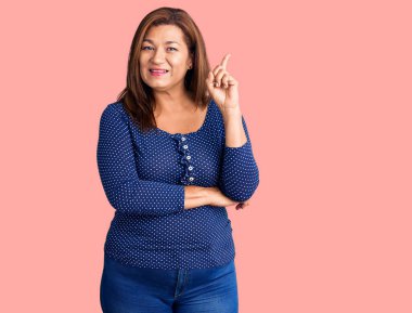 Orta yaşlı, sıradan kıyafetler giyen güzel bir kadın parmaklarını havaya kaldırmış, parmaklarını yana doğru uzatmış, mutlu yüzlü bir kadın..