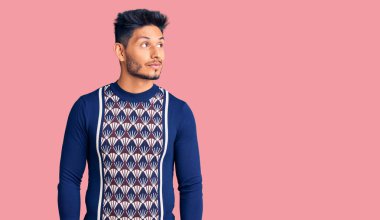 Yakışıklı Latin Amerikalı genç adam, günlük kışlık süveter giyiyor. Gülümsüyor, yan tarafa bakıyor ve düşünüyor.. 