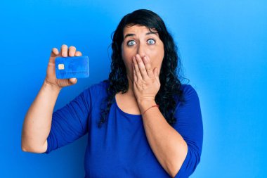 Ayrıca elinde kredi kartıyla ağzı kapalı, şok olmuş ve hata yapmaktan korkan esmer bir kadın. şaşırmış ifade 