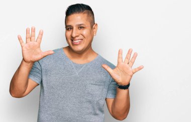 Gündelik kıyafetler giyen genç latin adam on numarayı gösterip işaret ederken kendinden emin ve mutlu gülümsüyor.. 