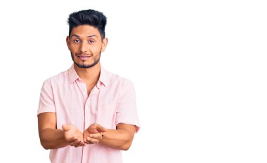 Yakışıklı Latin Amerikalı, sıradan bir yaz tişörtü giymiş, elleri avuçlarında gülümseyen, el hareketi yapan bir genç. Bekleme ve koruma 