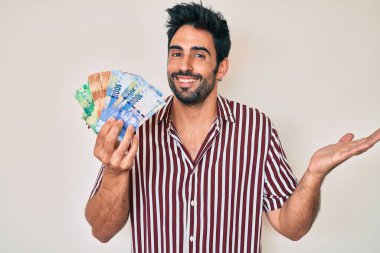 Sakallı yakışıklı İspanyol adam Güney Afrika rand banknotları tutuyor başarıyı mutlu bir gülümsemeyle kutluyor ve kazanan el kaldırarak ifade ediyor 