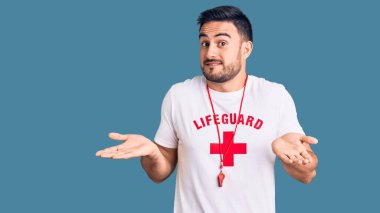 Genç yakışıklı adam cankurtaran üniforması giyiyor. Kolları ve elleri havada, kafası karışmış bir ifade. şüphe kavramı. 