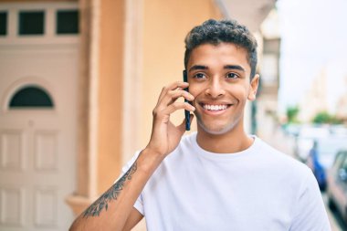 Genç Latin adam gülümsüyor ve şehirde akıllı telefondan konuşuyor..