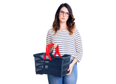 Süpermarket alışveriş sepeti tutan güzel, genç esmer bir kadın. Düşünme tavrı ve ayık bir ifade. Kendine güveni olan. 