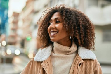 Genç Afrikalı Amerikalı kadın gülümseyerek şehirde mutlu mesut duruyor..