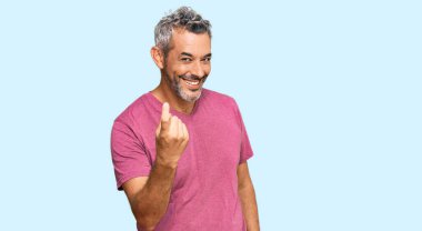 Orta yaşlı, gri saçlı, sıradan giyinmiş bir adam, el kol hareketi yaparak, mutlu bir şekilde karşılamaya ve gülümsemeye davet ediyor. 