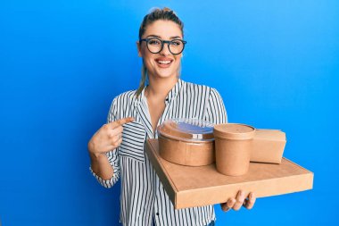 İş stili giyinen beyaz bir kadın elinde yiyecek teslimatı yaparken mutlu bir şekilde elini ve parmağını gösterdi. 