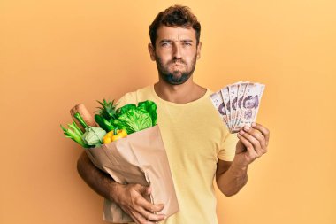 Sakallı yakışıklı bir adam market alışverişi yapıyor ve 500 Meksika pezosu komik suratıyla yanaklarını şişiriyor. Ağzı havayla şişer, havayı yakalar.. 