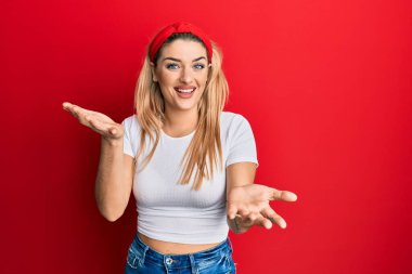 Beyaz günlük tişört giyen genç beyaz kadın güler yüzlü, kolları açık, dostça karşılama, olumlu ve kendinden emin selamlar. 