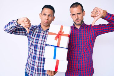 Kızgın suratlı, negatif işaretli, baş parmakları aşağıda, reddedilme kavramından hoşlanmayan iki genç gay erkek hediye tutuyor. 