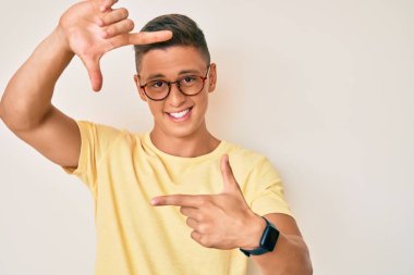 Gündelik kıyafetler ve gözlük takan, gülümseyen, elleri ve parmakları gülen yüzlü genç İspanyol çocuk. yaratıcılık ve fotoğrafçılık kavramı. 