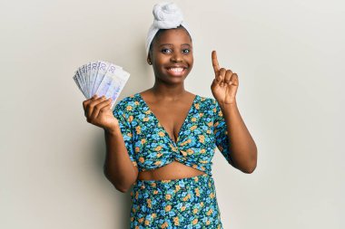 Saç sarığı takan genç Afrikalı bir kadın elinde 20 İsveç banknotuyla bir fikir veya soruyla gülümsüyor. 