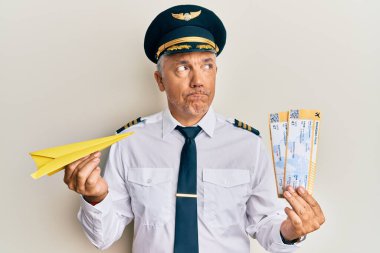 Yakışıklı, olgun bir pilot, elinde kağıt uçak ve uçuş kartı var. Gülümsüyor ve başka tarafa bakıyor.. 