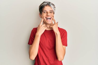 Gündelik kıyafetler giymiş, ağzı açık gülümseyen, parmakları işaret eden ve neşeli gülümsemeye zorlayan genç İspanyol bir adam. 