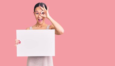 Güzel esmer, boş pankart tutan genç bir kadın gülümsüyor. Mutluluktan gülümsüyor. 