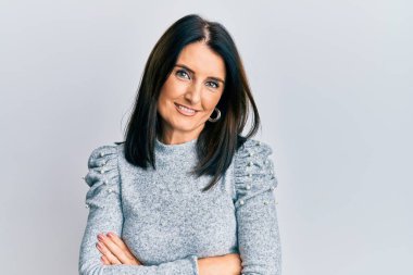 Orta yaşlı esmer, sıradan kıyafetler giyen mutlu yüzlü, kollarını kavuşturup kameraya bakan bir kadın. pozitif kişi. 