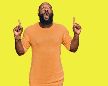 Gündelik giysiler giyen genç Afro-Amerikan adam şaşkın ve şaşırmış bir şekilde yukarı baktı ve parmaklarıyla işaret etti ve kollarını kaldırdı.. 