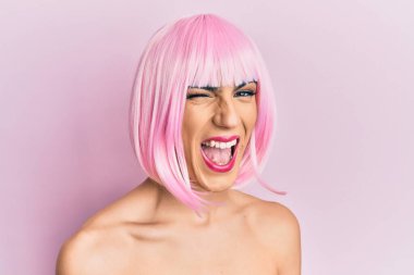 Pembe peruk takmış genç bir adam kameraya seksi bir ifadeyle bakıyor, neşeli ve mutlu bir yüzle.. 