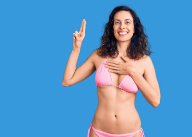 Genç ve güzel İspanyol kadın bikini giyip gülümsüyor. Göğsü ve parmakları havada küfür ediyor. Sadakat yemini ediyor. 