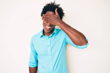 Yakışıklı Afro saçlı, sıradan kıyafetler giyen, gülümseyen ve yüzünde şaşkınlıktan gözleri kapayan afro-amerikalı bir adam. kör kavram. 