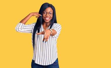 Gündelik kıyafetler ve gözlük takan, gülümseyen genç Afro-Amerikalı kadın telefon jesti üzerine konuşarak seni işaret ediyor. Ara beni.. 