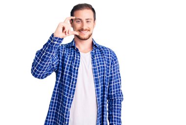 Genç, beyaz, günlük kıyafetler giyen, gülümseyen, kendine güvenen, el hareketi yapan, parmaklarıyla işaret yapan ve kameraya bakan yakışıklı bir adam. ölçüm kavramı. 