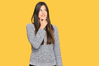 Genç esmer kadın, sıradan bir kazak giyiyor, elleri çenesinde soru soruyor, düşünceli bir yüz ifadesi var. Düşünceli bir yüzle gülümsüyor. şüphe kavramı. 