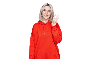 Gündelik kıyafetler giyen genç sarışın kız üç numarayı gösterip işaret ederken kendinden emin ve mutlu gülümsüyor.. 