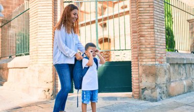Sevimli Latin öğrenci çocuk ve anne şehirde yürüyor. Çocuk elleriyle gözlük hareketi yapıyor..