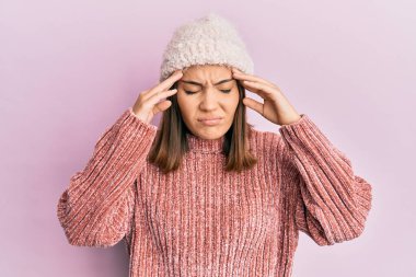 Genç, güzel bir kadın yün kazak giyiyor ve elinde kafasıyla kış şapkası takıyor. Stres yüzünden baş ağrısı çekiyor. migren ağrısı. 