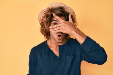 Yaz şapkası takan genç İspanyol adam şok içinde yüzünü ve gözlerini kapayarak utangaç ifadesiyle parmaklarının arasından bakıyor.. 